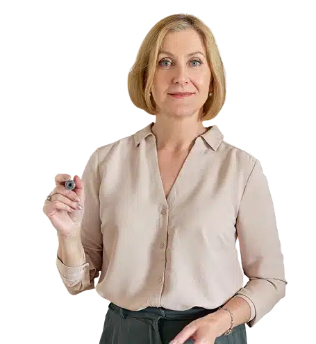 A woman with short blonde hair, wearing a light beige blouse, stands facing forward and holds a marker in her right hand, as if ready to write or draw.