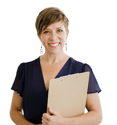 Smiling woman with short brown hair wearing a navy blue dress, holding a clipboard, standing against a white background.