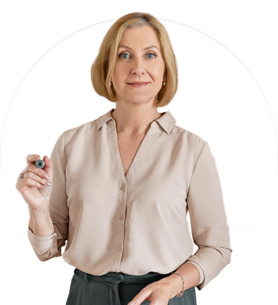 A woman with short blonde hair, wearing a light pink blouse and dark pants, holds a marker and looks at the camera, standing in front of a white circular background.