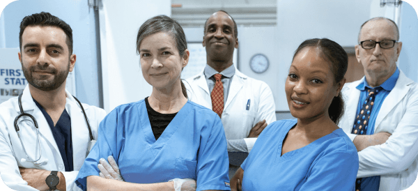 Five medical professionals, including men and women of diverse backgrounds, stand confidently together in a hospital setting, wearing scrubs and white coats, with stethoscopes and medical badges visible.