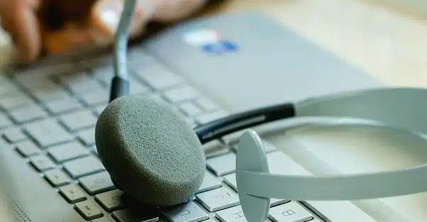 A close-up of a computer keyboard with a headset resting on it, while a person's hand types in the background.