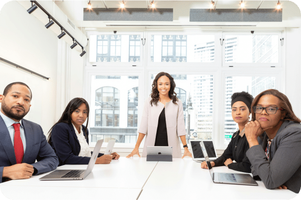 Five professionals, representing leading Sage Intacct partners, sit and stand around a conference table with laptops and tablets, posing for a meeting in a bright office with large windows and a cityscape view in the background.