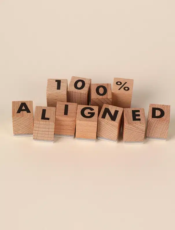Stacked wooden blocks spell out "100% ALIGNED" against a neutral background.