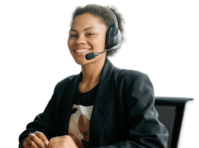 A smiling Replicon expert wearing a headset sits at a desk, dressed in a black blazer and patterned shirt, ready to assist project based businesses, against a plain white background.