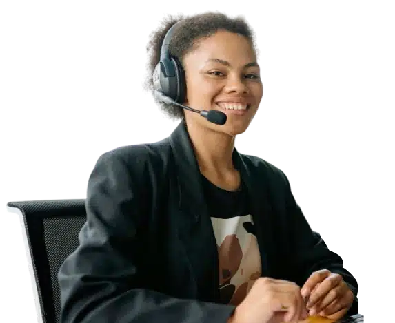 Smiling woman wearing a headset sits at a desk, dressed in a black blazer and patterned shirt, ready to assist as a customer service representative.