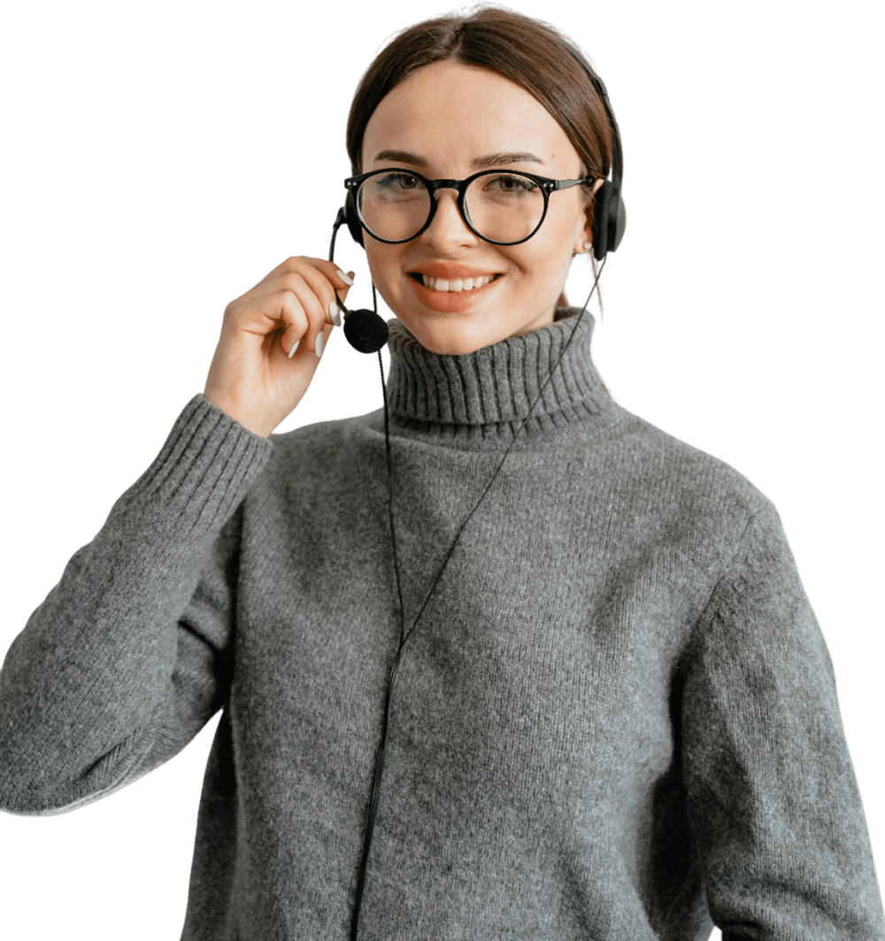 A smiling woman wearing glasses and a gray sweater uses a headset with a microphone, ready to assist you with project cost management software, standing against a plain white background.