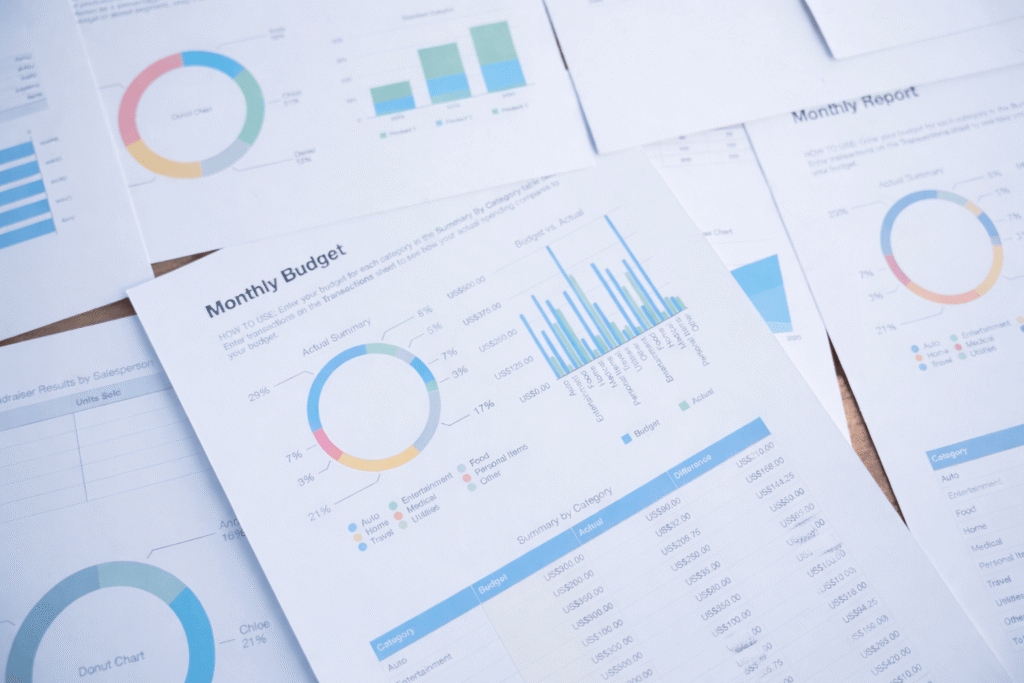 Documents with colorful pie charts, bar graphs, and tables showing financial data and summaries are spread across a desk. The main page is titled "Monthly Budget," highlighting the importance of accurate financial statements for managing expenses.