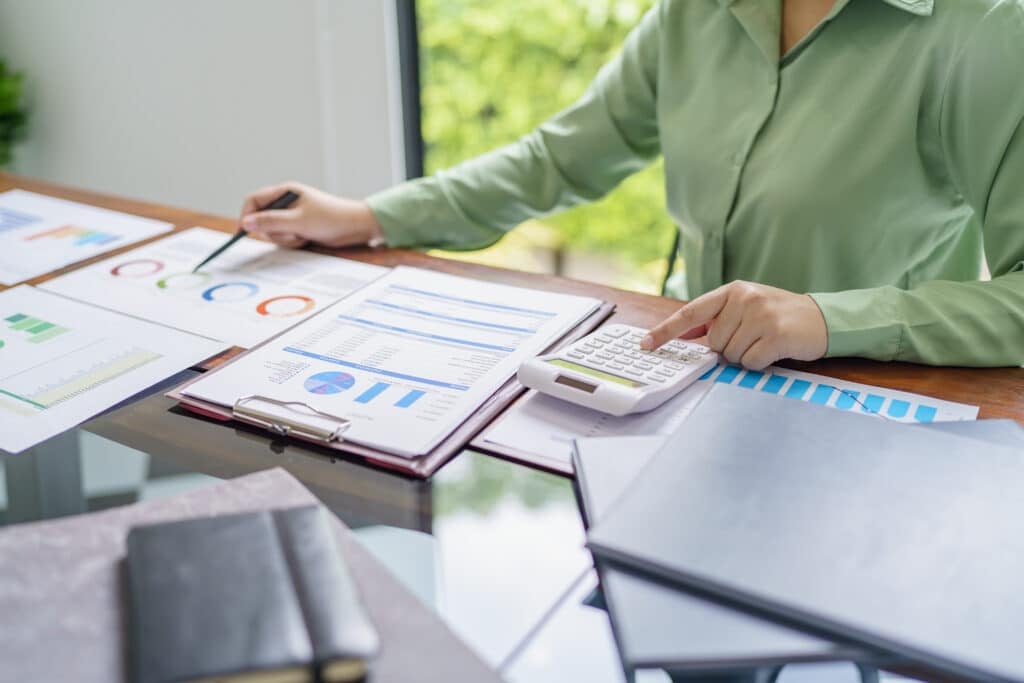 A person in a green shirt sits at a desk analyzing financial charts and graphs, using a calculator and reviewing documents related to financial reporting with data and colorful graphs.