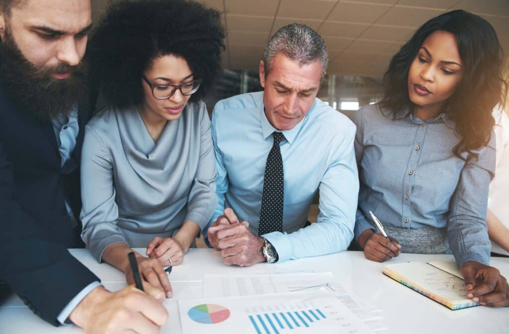 Four business professionals, three women and one man, are gathered around a table reviewing documents and charts. They appear focused as they discuss financial statements and address concerns about financial reporting errors.