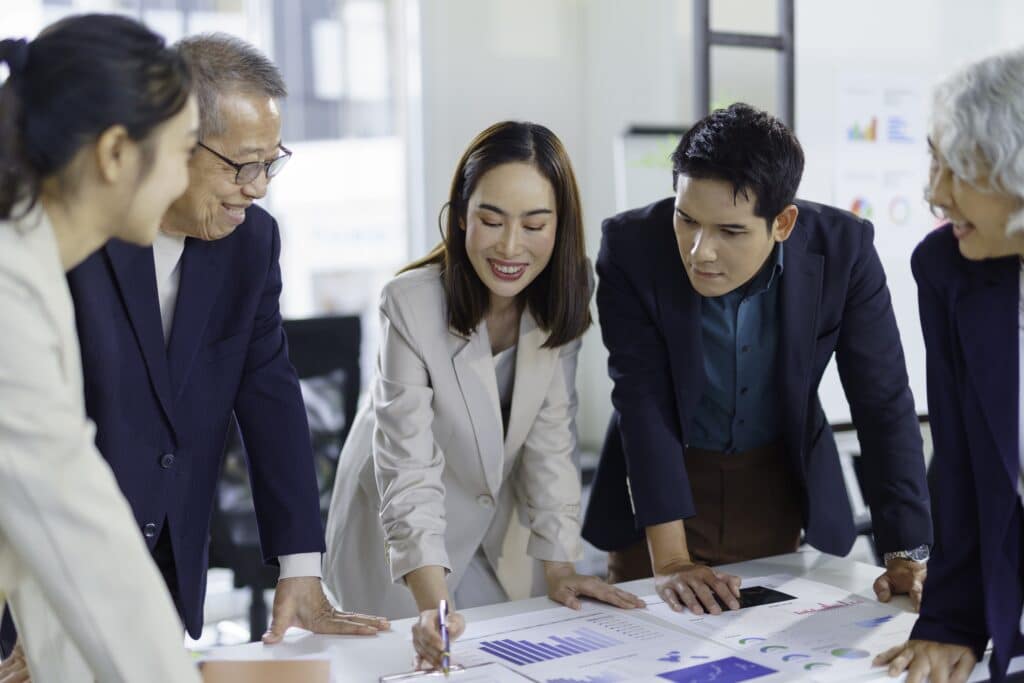 Group of businesspeople leaning over a table, examining financial charts and discussing data during a productive meeting in the office