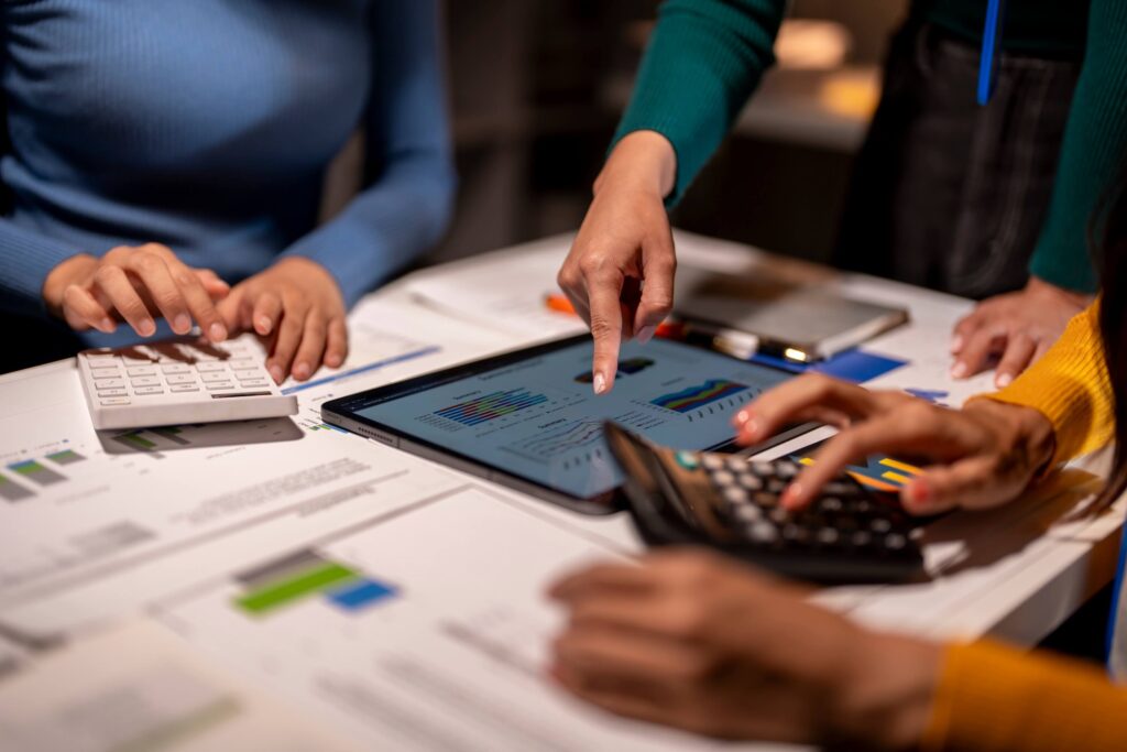 Three people working together at a desk with charts, a tablet displaying graphs, and calculators, collaborating on cash flow forecasting and business data analysis.