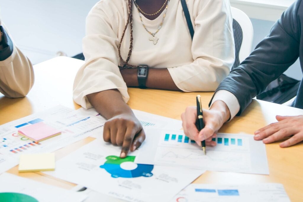 Two people sit at a table reviewing papers and charts with graphs and data; one points to a chart while the other writes, discussing accounting guidance from the Financial Accounting Standards Board and referencing ASU 2018-08.