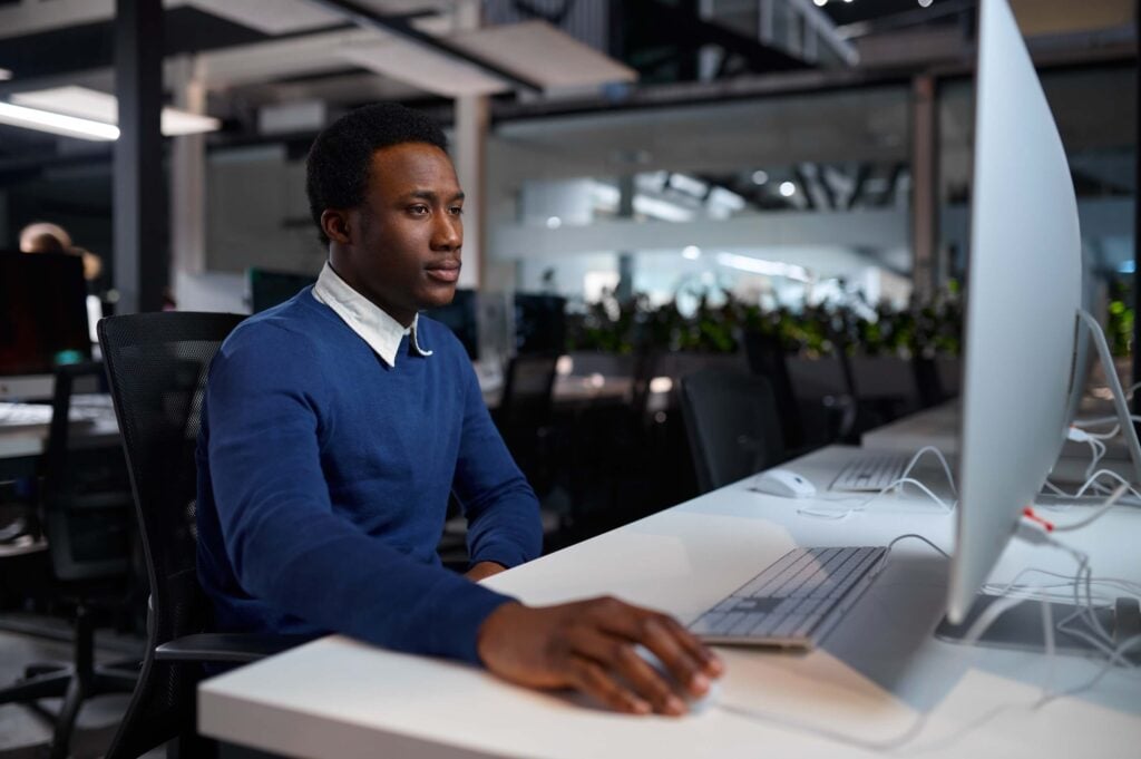 A man in a blue sweater sits at a desk working on a computer in a modern office with a focused expression, as he integrates the Sage Intacct API into his workflow.