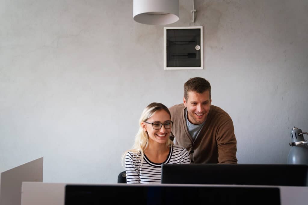 A woman and man smiling while looking at a Sage 100 upgrade on a computer screen in an office.