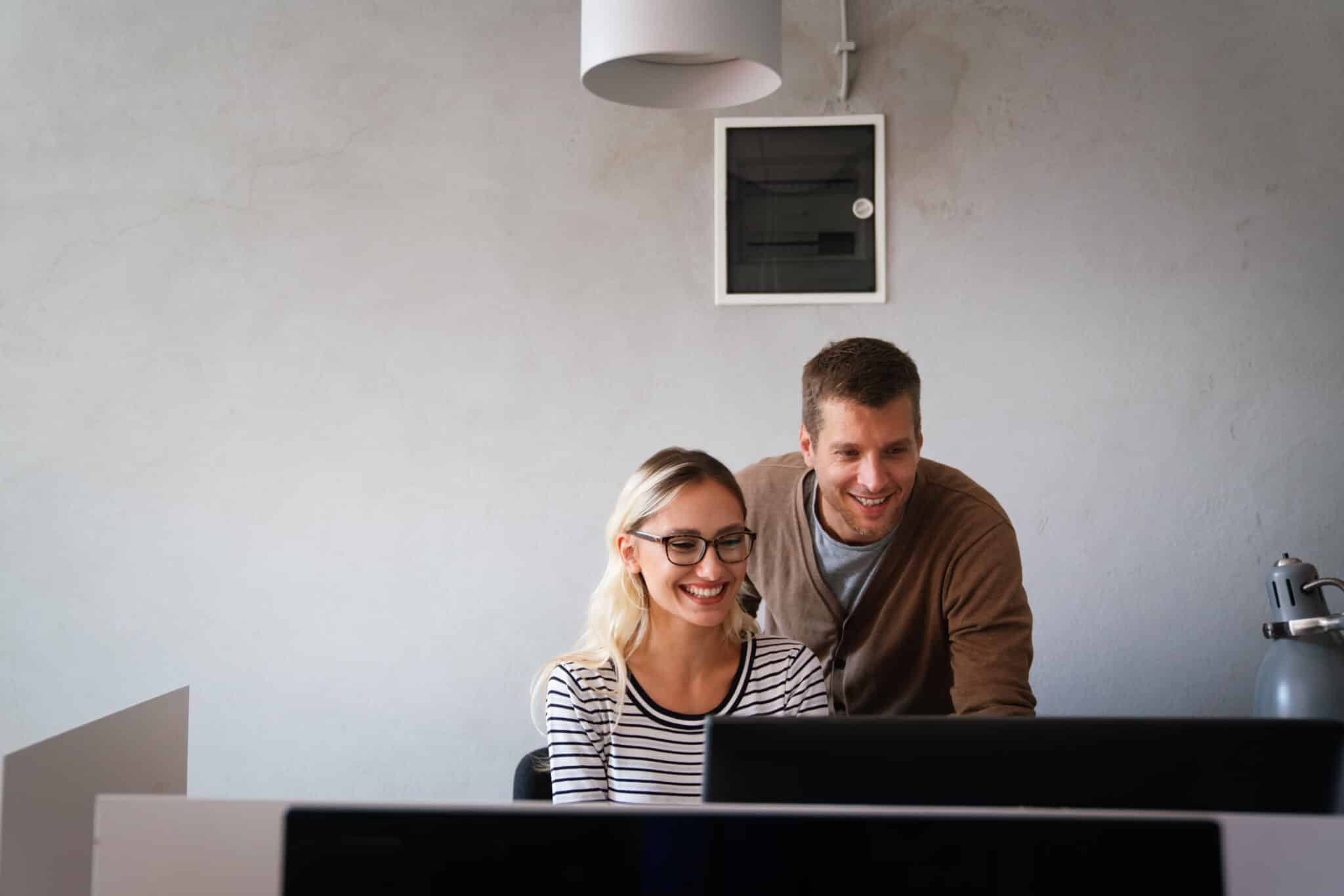 A woman and man smiling while looking at a Sage 100 upgrade on a computer screen in an office.